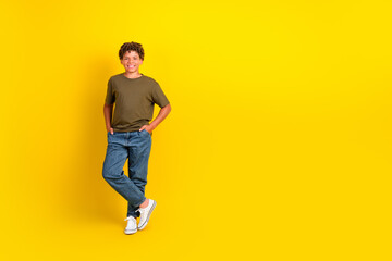 Obraz premium Bright happy boy in casual khaki t shirt and jeans poses against a bold yellow background for a playful lifestyle stock image