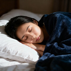 A woman sleeping peacefully on a white pillow covered with a blue blanket in a well lit bedroom