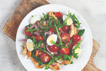 a warm salad with fried chicken fillet, arugula and cherry tomatoes, and boiled quail eggs, on a white plate, no people.