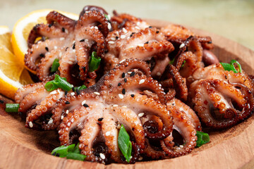 grilled baby octopus with green onions, lemon slices, on a wooden plate, homemade, no people,