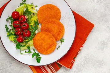 crispy fried fish cutlets, fish burgers, on a white plate, with fresh lettuce leaves, arugula and cherry tomatoes, homemade, no people,
