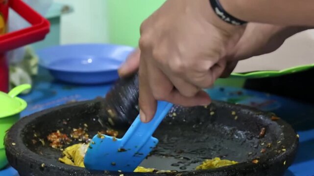 Close-up of traditional Indonesian street food preparation using a stone mortar and pestle, grinding sambal and seasoning for authentic local flavor.