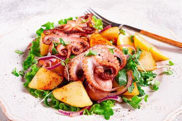 Grilled octopus with baked potatoes and fresh herbs, on a decorative light plate, homemade, no people