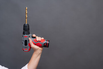 Cordless drill with long bit held in hand raised, power tool raised isolated neutral background, professional equipment. Hand holding cordless drill with extended drill bit, modern power tool isolated