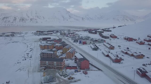 Drone flight forward. Aerial view of Longyearbyen city, Svalbard in winter. Landscape with mountains and colorful houses. Image in D-log without color correction.