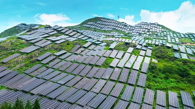 Aerial shot of a vast solar power plant with panels covering green hills.