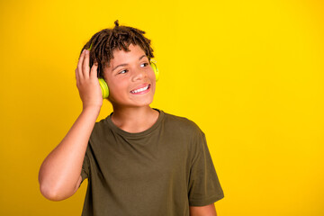 Playful teen smiles while wearing green headphones and enjoying music against a bright yellow background in casual style stock image