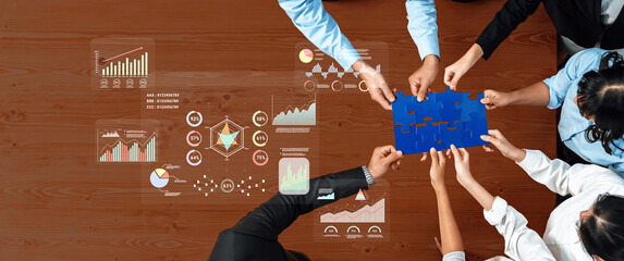 Diverse professionals engage in teamwork, collaborating over a blue puzzle piece and digital charts, demonstrating strategic planning and problem-solving in a business environment. Trope