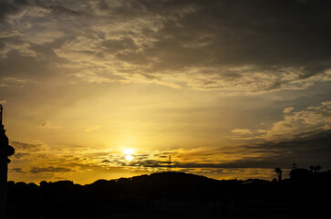 Golden Sunset Over Silhouetted Hills and City Skyline with Dramatic Cloudy Sky