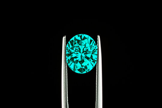A close up of a paraiba tourmaline in jewelry tweezers