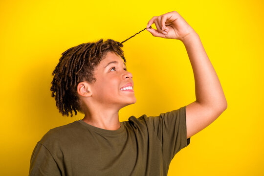 playful young boy pulls a strand of hair against a bright yellow background wearing a casual khaki t shirt for a fun stylish lifestyle promo