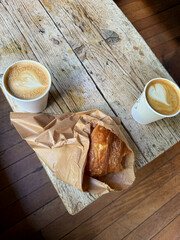 Two cups of latte with heart art and a croissant on a rustic wooden table.