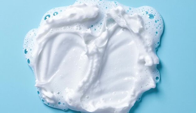Face cleansing mousse smudge sample. White cleanser or soap foam bubbles on blue background. Shower gel, hair shampoo foam smear texture.