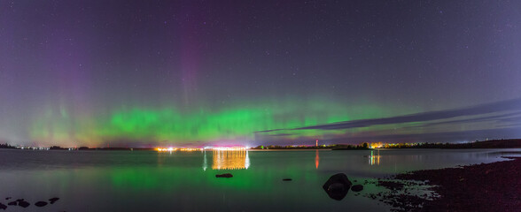 The aurora borealis over the lake. The city lights glow in the distance.