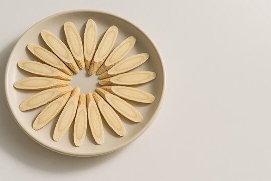 Dried astragalus root slices neatly arranged in a circular pattern on a ceramic plate in soft natural lighting.