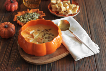 Creamy pumpkin soup with croutons and seeds, served in a pumpkin-shaped bowl on dark wooden table.
