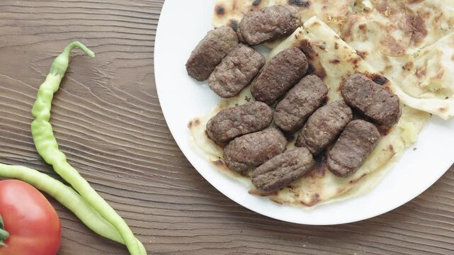 Close-Up of Romanian Mici Sausages Served with Flatbread and Tomatoes on a White Plate	