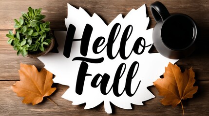 Coffee mug sits on a wooden table with a leaf and a potted plant. The leaf is a large, white leaf with black writing that says "Hello Fall." The coffee mug is black