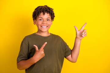 Funny bright boy with dreadlocks points to the right wearing khaki tshirt against a bold yellow...