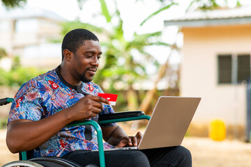 African Man in Wheelchair Making Online Payment with Credit Card and Laptop