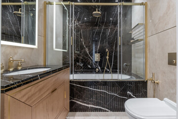 A stylish bathroom decorated with dark marble, with a spacious bathtub and gold fittings. The elegant dressing table complements the high-end design.