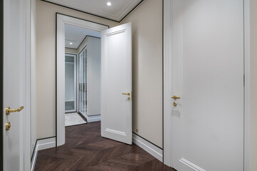 A modern entrance hall with elegant white doors with gold handles, luxurious wooden floors and minimalist design.