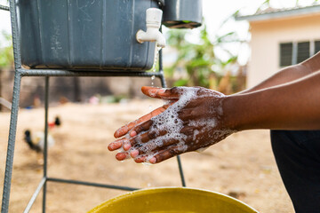 African man in wheelchair washing hands with Veronica bucket outdoors for hygiene and disease prevention