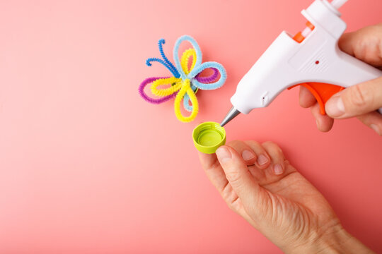 Crafting moment with hot glue gun and colorful pipe cleaner butterfly on pink background, ideal for educational content, DIY kits, kids activity brands, creative learning visuals,