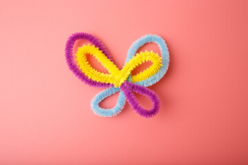 Colorful pipe cleaner butterfly on pink background, ideal for children craft tutorials, preschool education, DIY kits, and playful branding in eco-friendly or creative industries