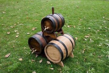 Three small wooden barrels with metal hoops and brass taps arranged on a green lawn. Traditional oak casks used for aging wine, whiskey, or beer, displayed outdoors in a rustic setting.