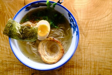 Bowl of Japanese ramen noodles with egg, pork, and seaweed on wooden table