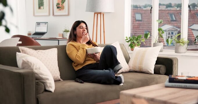 Laughing, popcorn and watching tv with woman on sofa in living room of home for streaming. Comedy, eating and entertainment with happy Indian person in apartment for video subscription service