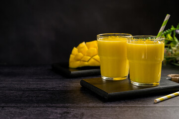 Mango banana smoothie in a glass with fresh fruit, black background, copy space