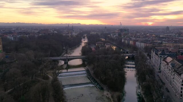 4K Drohnenflug &uuml;ber die Isar in M&uuml;nchen bei Sonnenuntergang mit Alpenpanorama und Skyline mit Deutschem Museum, Landtag, Gasteig, Maximilianbr&uuml;cke und St. Lukas.
