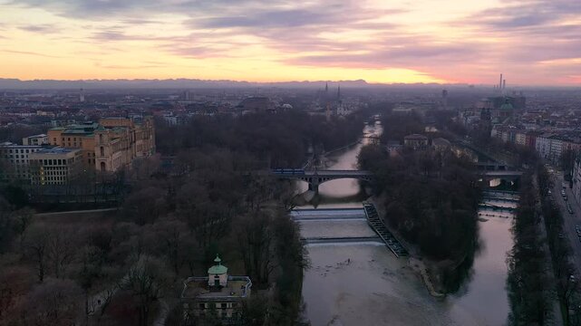 4K Drohnenflug &uuml;ber die Isar in M&uuml;nchen bei Sonnenuntergang mit Alpenpanorama und Skyline mit Deutschem Museum, Landtag, Gasteig, Maximilianbr&uuml;cke und St. Lukas.