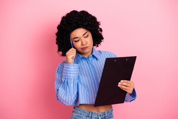 Young woman with clipboard thinking over decisions while standing against pink background