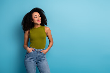 Confident young woman with curly hair in casual green top against a vibrant blue background exuding...