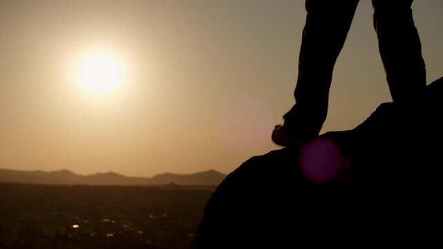 Silhouette of man hiker extending helping hand to friend while climbing mountain
