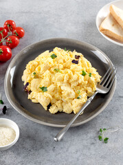 Scrambled eggs with green onions, tomato, cheese on a gray plate on gray background. Healthy breakfast. 