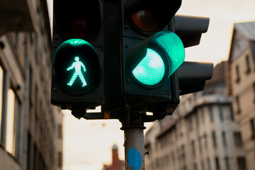 Traffic lights showing green pedestrian walk signal and green car light at city intersection surrounded by European buildings, symbolizing coordinated urban movement and safety system