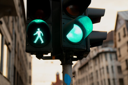 Traffic lights showing green pedestrian walk signal and green car light at city intersection surrounded by European buildings, symbolizing coordinated urban movement and safety system - Powered by Adobe