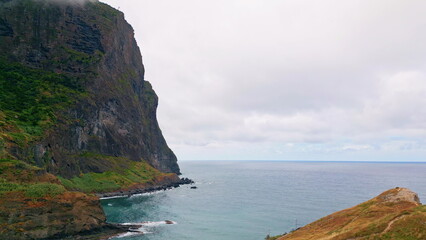 Fototapeta premium Tall rock standing shoreline aerial view. Waves crashing stone under cloudy sky.