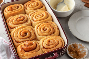 Freshly baked cinnabon buns in a ceramic baking dish on light gray background. Making cinnamon rolls process