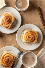 Freshly baked cinnabon roll buns served on ceramic plates with coffee on brown textured background. Cozy autumn breakfast concept. Top view