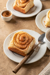 Freshly baked cinnabon roll buns served on ceramic plates with coffee on brown textured background. Cozy autumn menu concept