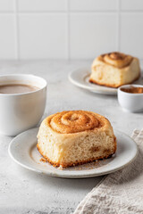 Freshly baked cinnabon bun on ceramic plate and coffee for breakfast on light gray background. Menu, autumn food concept