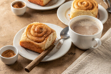 Freshly baked cinnabon roll buns served on ceramic plates with coffee on brown textured background. Cozy autumn menu concept
