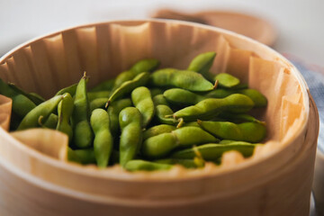 Steamed edamame soybeans in a bamboo basket with soft natural lighting, showcasing healthy Japanese appetizer and vegan snack concept in minimalist composition