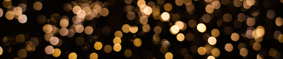 Extra wide panorama banner of blurry golden fairy string lights in dark, beautiful bokeh effect with glowing circles or shiny dots, abstract holiday banner for website, landing page or newsletter