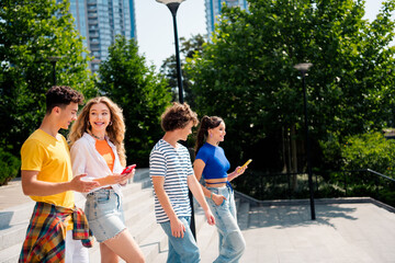 Young friends enjoying time together outdoors in a sunny city park, dressed casually, and using smartphones during summer.